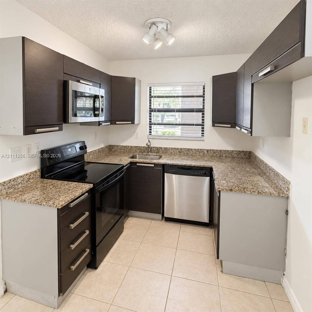 Kitchen featuring dark cabinetry, stone-finish countertops, stainless steel appliances, tile flooring, and multi-light ceiling fixture