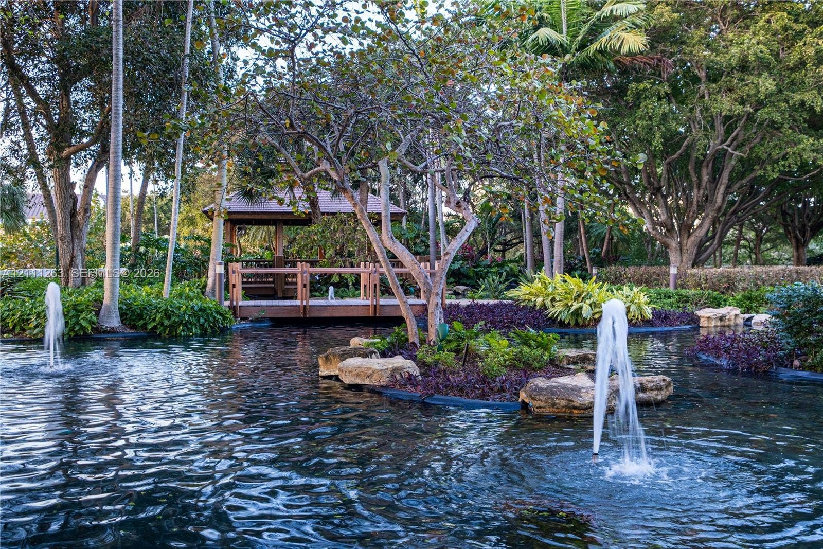 4000 Towerside Terrace, #604, Miami, FL 33138 Water feature with dual fountains, pond, wood-framed gazebo, mature trees, and landscaped stone edging