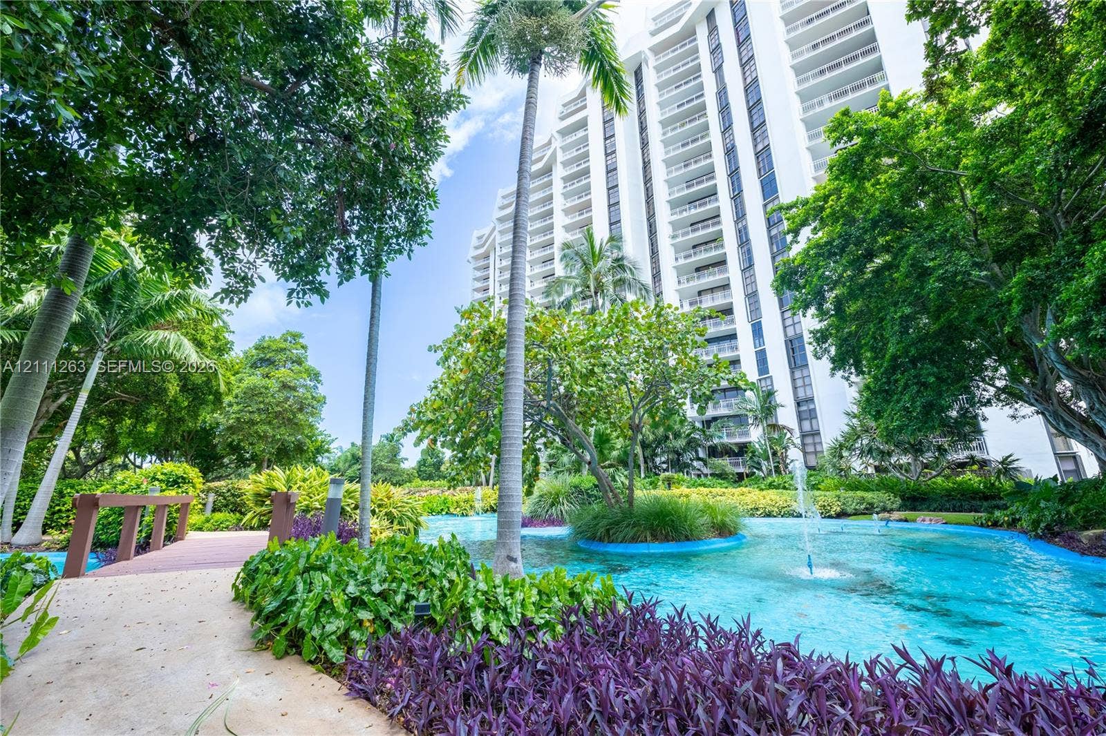 4000 Towerside Terrace, #604, Miami, FL 33138 Multi-story high-rise building featuring a landscaped courtyard with a decorative pond, integrated fountains, mature palm trees, and a pedestrian footbridge