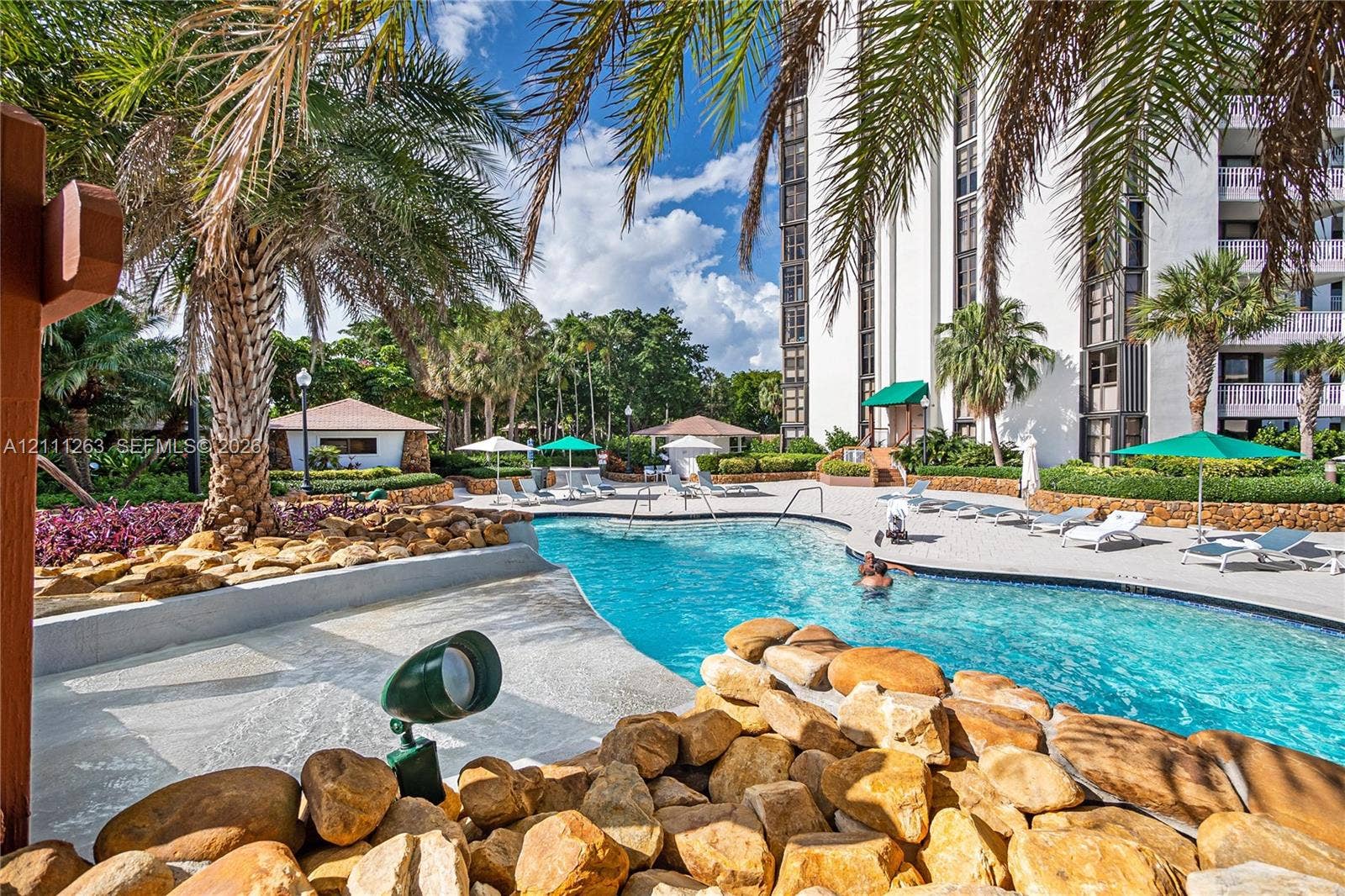 4000 Towerside Terrace, #604, Miami, FL 33138 Swimming pool featuring a sun shelf entry, natural stone hardscaping, tropical landscaping, and structural shade coverings