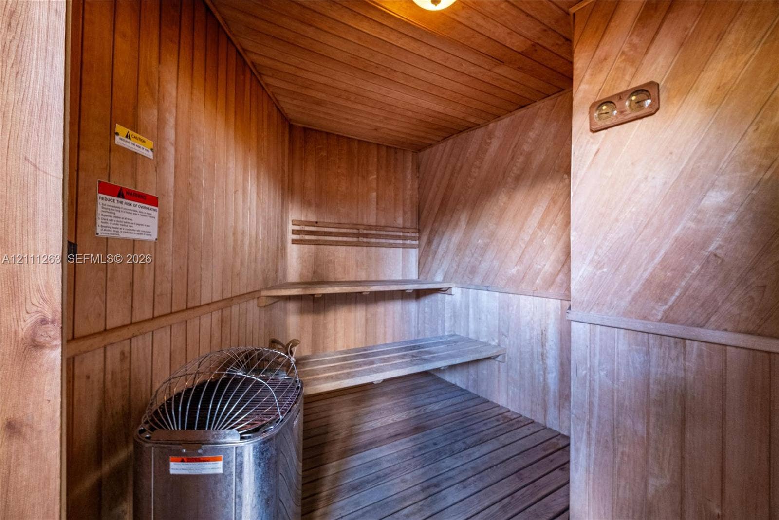 4000 Towerside Terrace, #604, Miami, FL 33138 Sauna interior featuring natural wood-paneled walls, built-in tiered wooden benches, slatted wood flooring, and a metal sauna heater with a protective cage