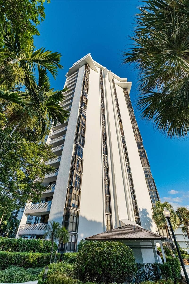 4000 Towerside Terrace, #604, Miami, FL 33138 High-rise residential exterior featuring a white stucco facade, vertical window banks, private balcony tiers, and mature palms