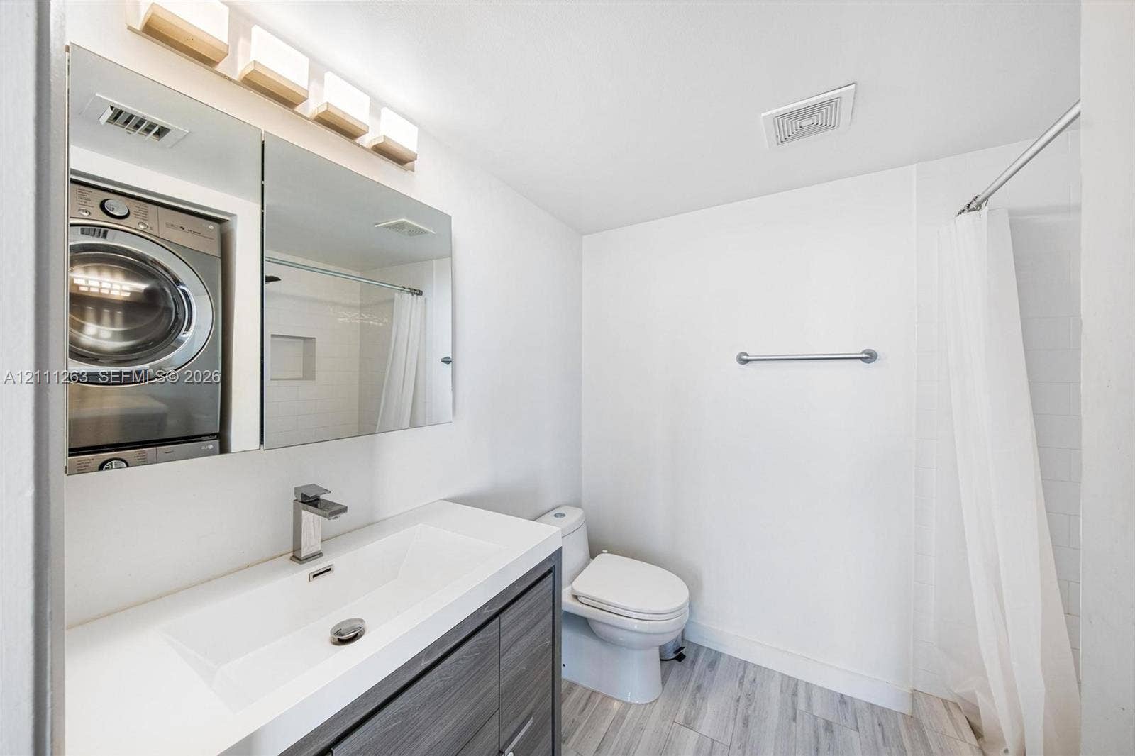 4000 Towerside Terrace, #604, Miami, FL 33138 Wood-finish vanity with integrated rectangular sink and metallic faucet, mirrored medicine cabinet, stacked laundry appliance, and shower with tiled surround