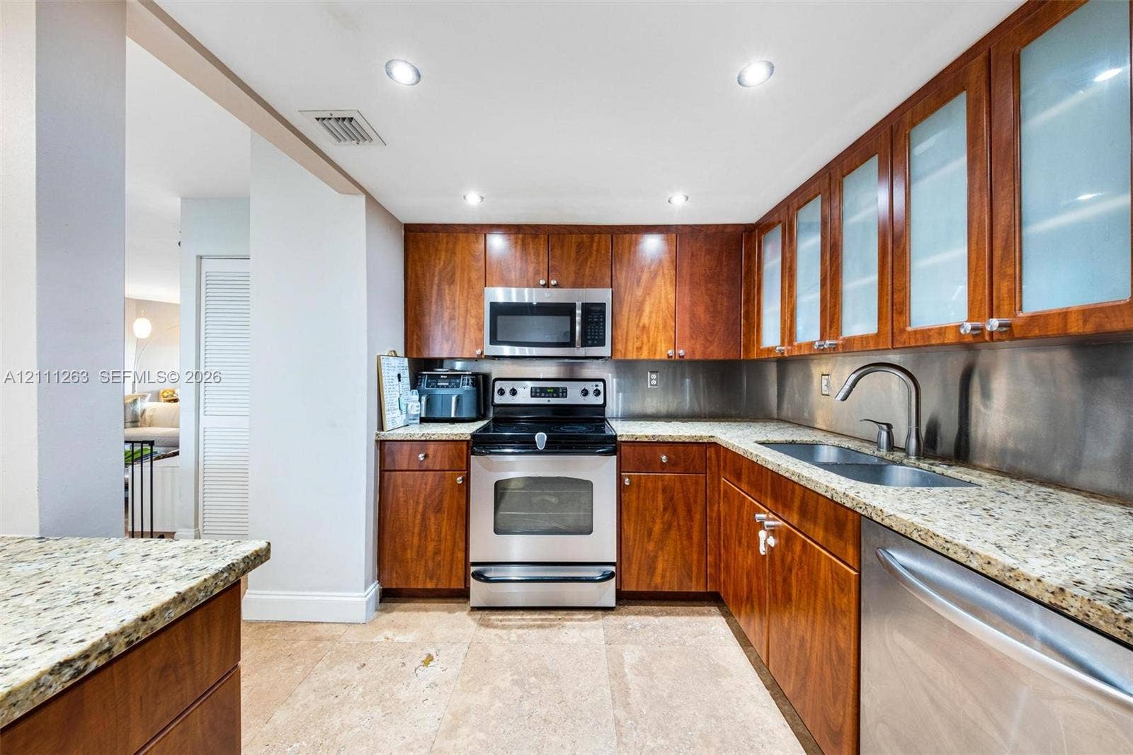 4000 Towerside Terrace, #604, Miami, FL 33138 Kitchen featuring wood cabinetry with glass-panel uppers, stone-finish countertops, stainless steel appliances, a metallic backsplash, and recessed lighting