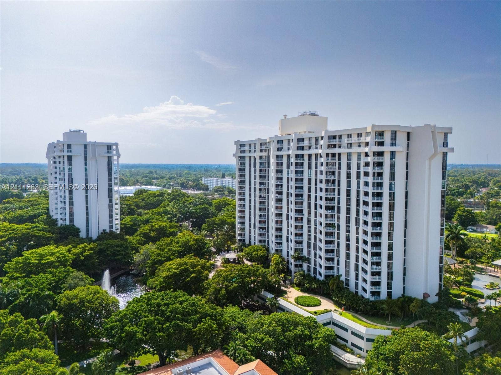 4000 Towerside Terrace, #604, Miami, FL 33138 High-rise residential towers surrounded by mature trees, landscaped grounds, pedestrian walkways, and a decorative water feature