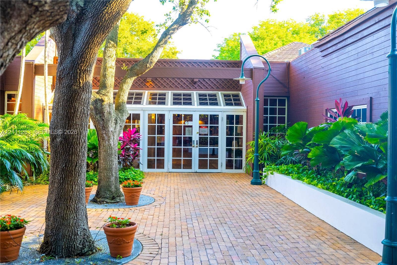 4000 Towerside Terrace, #604, Miami, FL 33138 Exterior entrance featuring a brick-paved courtyard, wood-paneled siding, a multi-pane glass double-door entryway, and mature landscape plantings