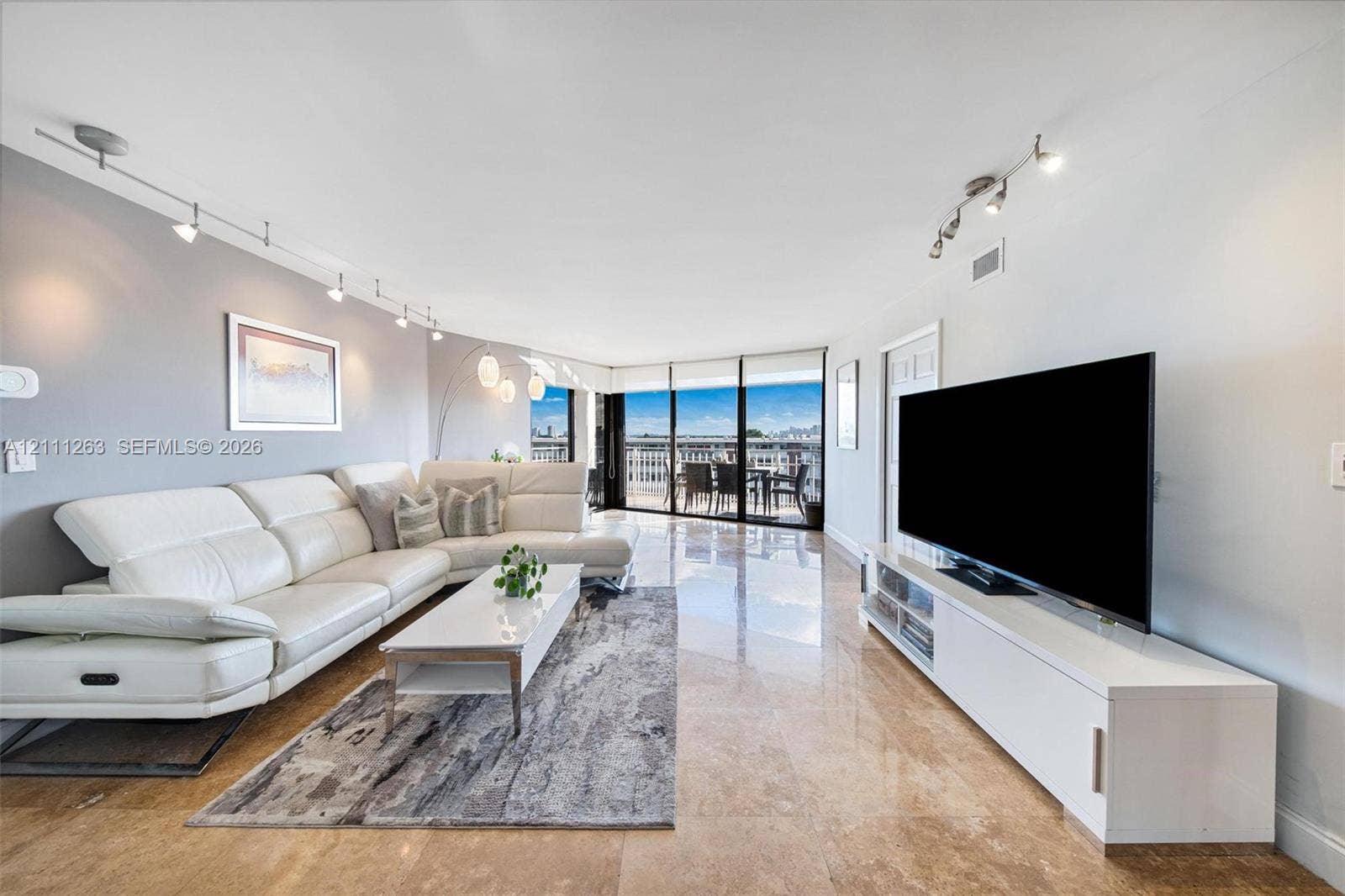 4000 Towerside Terrace, #604, Miami, FL 33138 Living space featuring polished stone flooring, floor-to-ceiling glass sliding doors, track lighting, and a painted accent wall