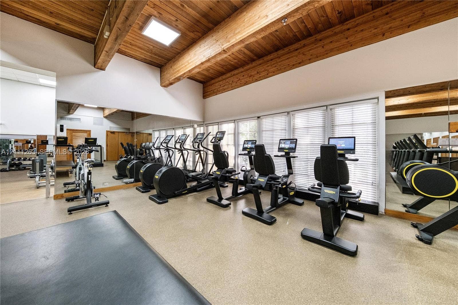 4000 Towerside Terrace, #604, Miami, FL 33138 Fitness room featuring vaulted wood-paneled ceilings, exposed structural beams, floor-to-ceiling wall mirrors, and large windows with integrated blinds