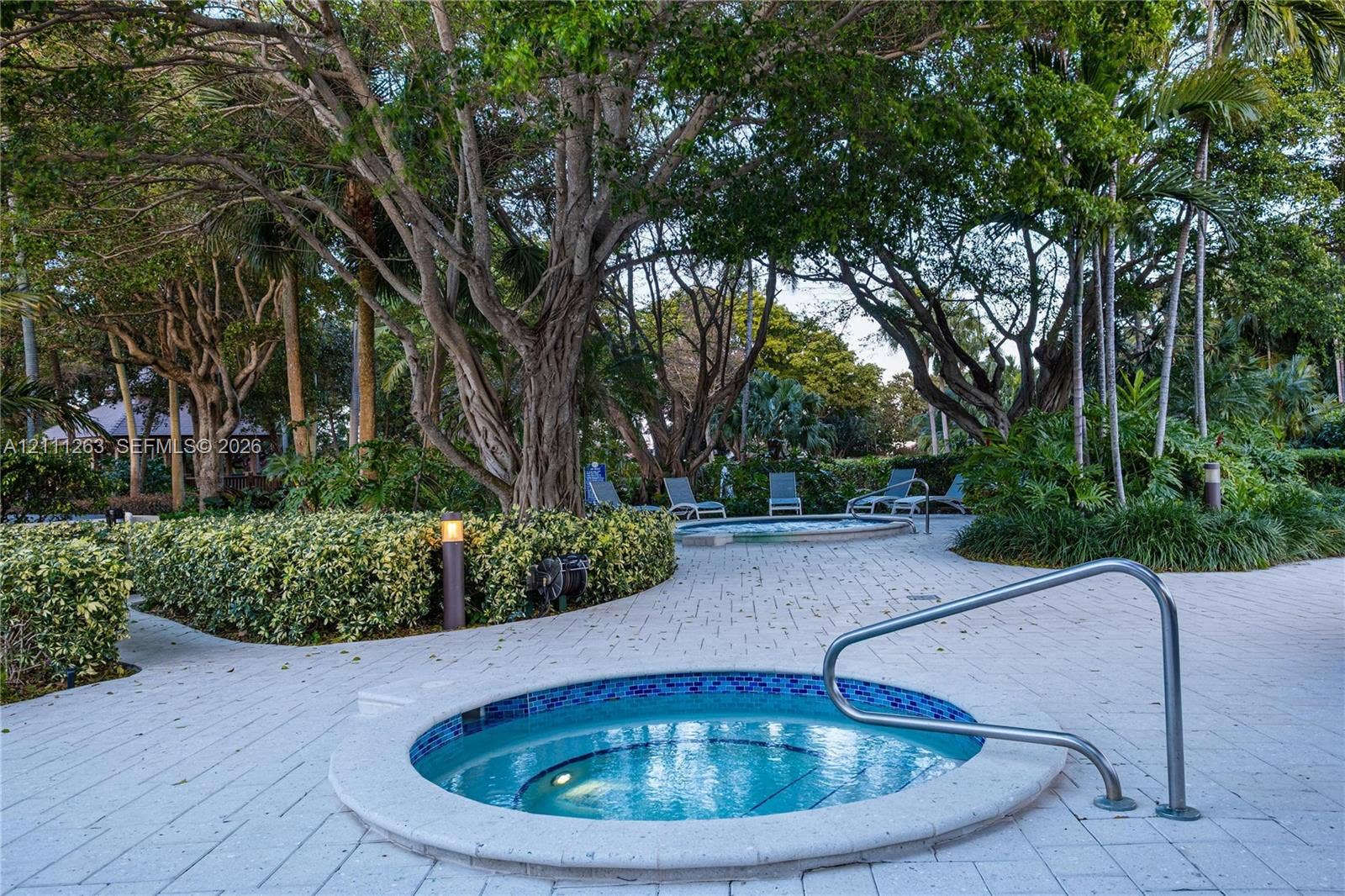 4000 Towerside Terrace, #604, Miami, FL 33138 In-ground spa with mosaic tile interior and integrated metal handrail, situated on a stone-paver deck surrounded by mature landscaping