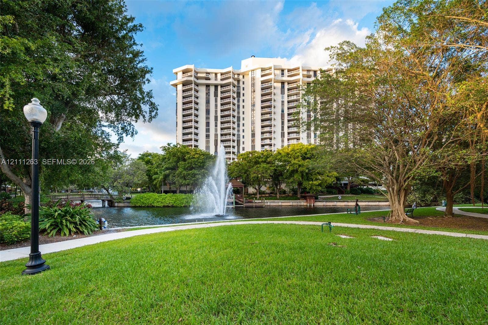 4000 Towerside Terrace, #604, Miami, FL 33138 High-rise residential exterior featuring private lake frontage, a central water fountain, landscaped grounds, and paved walking paths