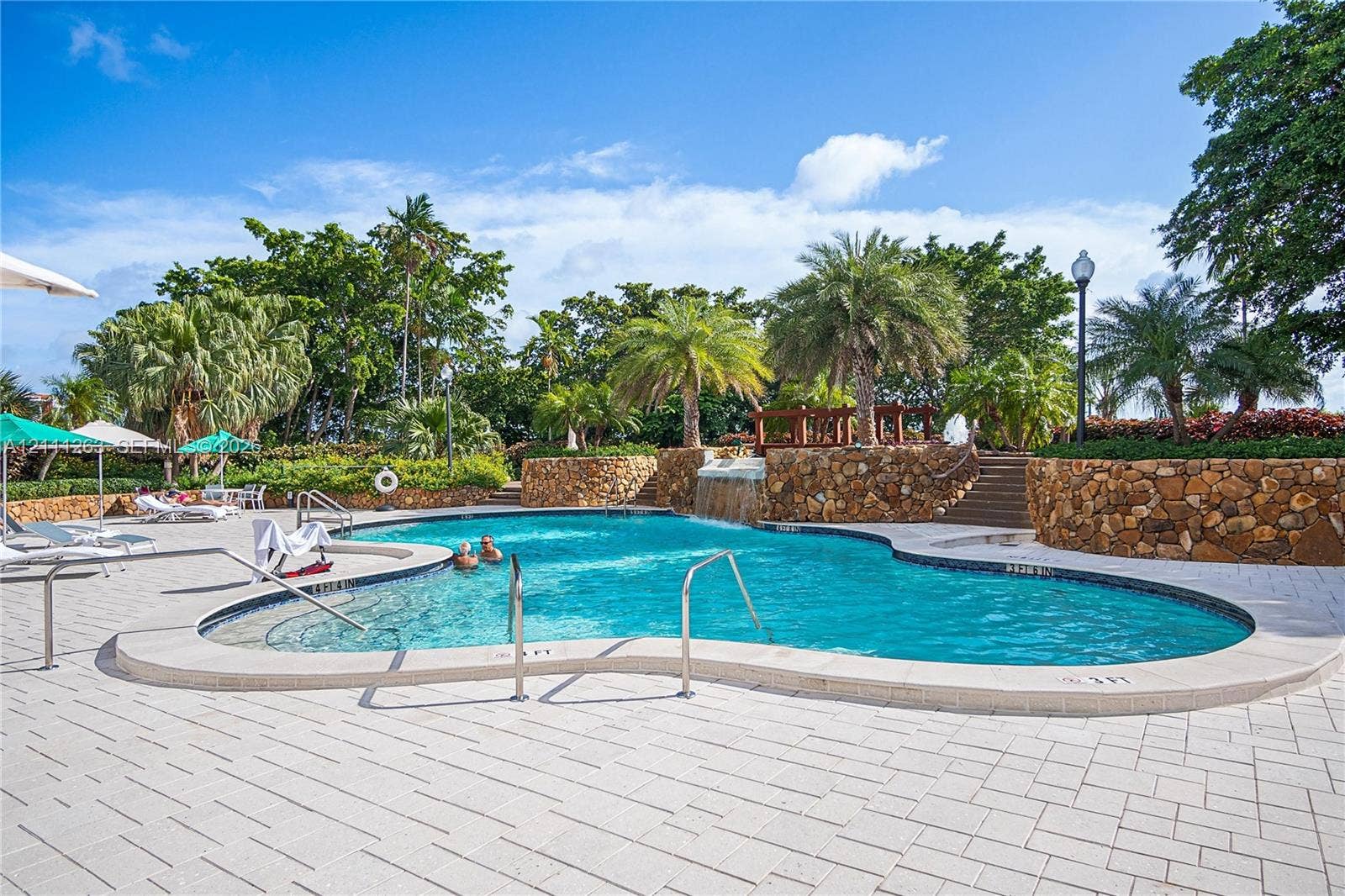 4000 Towerside Terrace, #604, Miami, FL 33138 Freeform pool with a water feature, stone retaining walls, paved deck, and mature palm landscaping