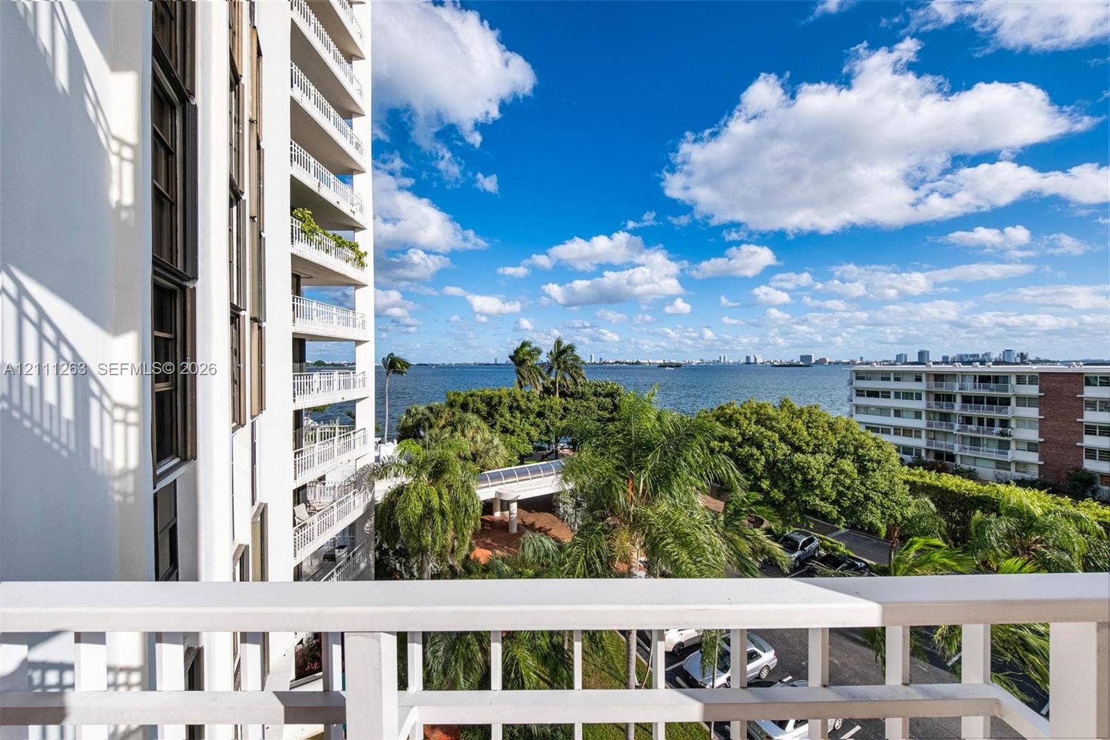 4000 Towerside Terrace, #604, Miami, FL 33138 Private balcony with white railing, featuring expansive water scenery, tropical landscaping, and mature palm trees