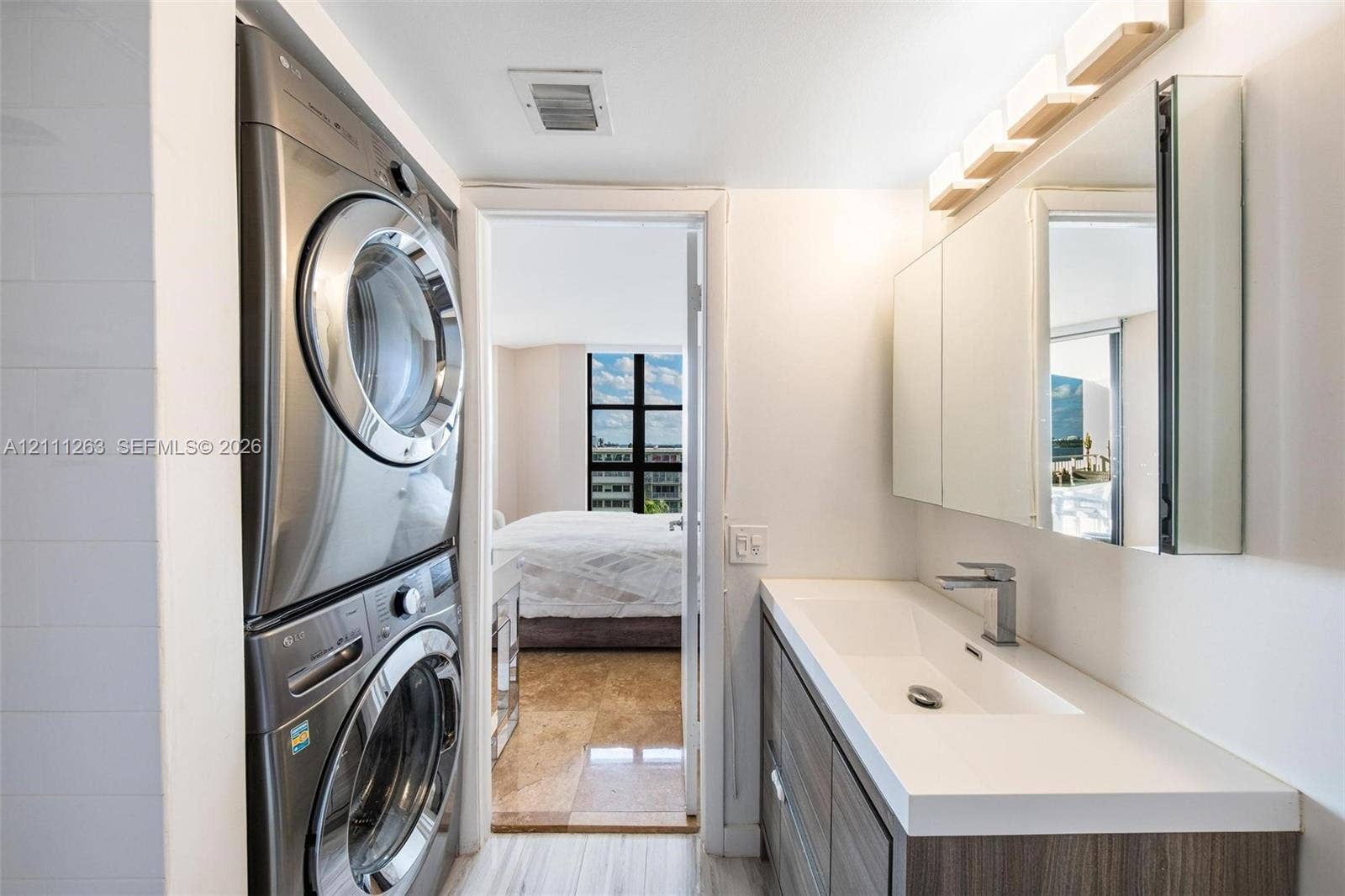 4000 Towerside Terrace, #604, Miami, FL 33138 Stacked front-loading laundry appliances, built-in vanity with integrated rectangular sink, quartz countertop, multi-panel mirrored medicine cabinet, and contemporary single-handle faucet