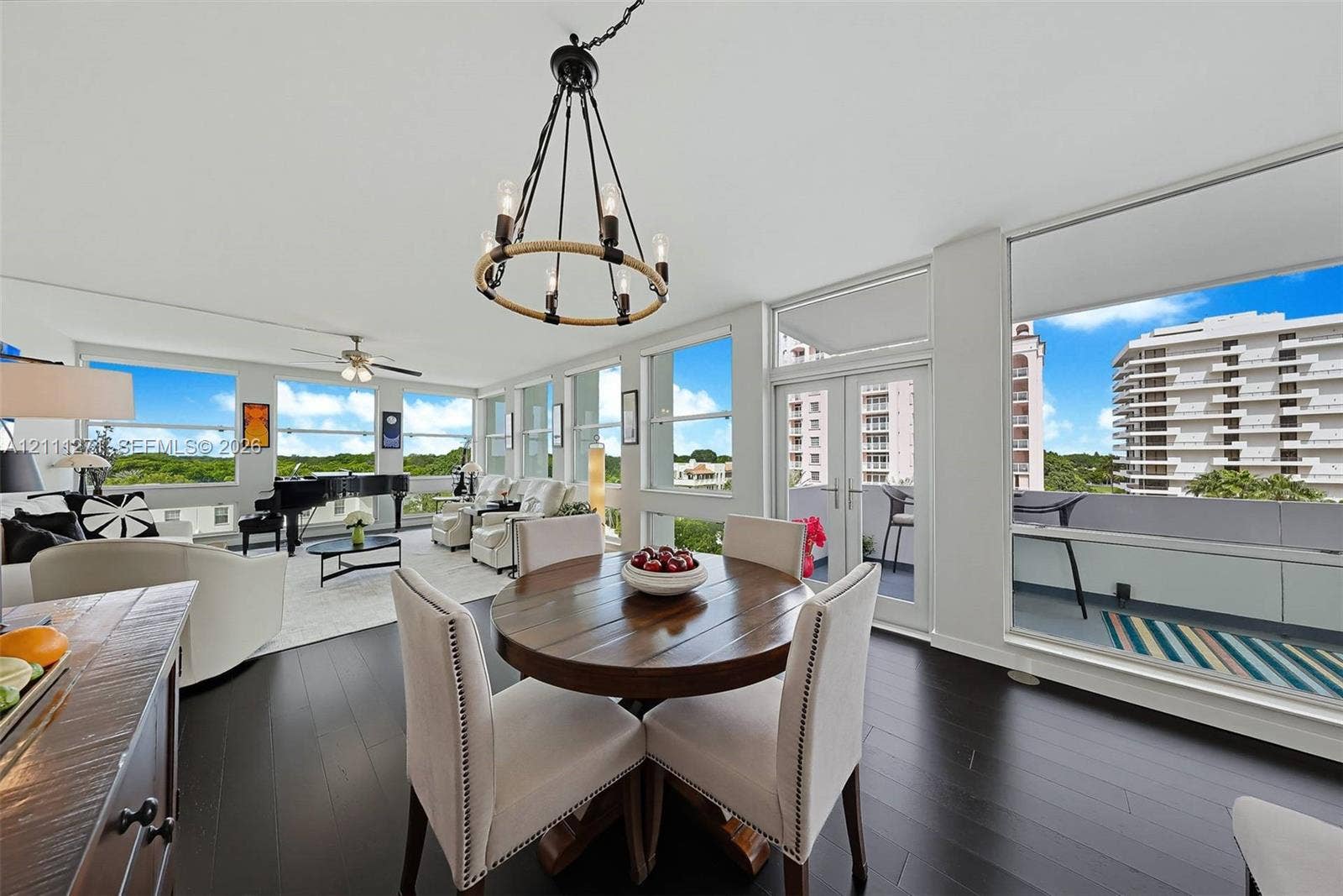 Living area featuring dark wood-finish flooring, a circular rope-accented chandelier, expansive floor-to-ceiling windows, and double glass doors opening to a balcony