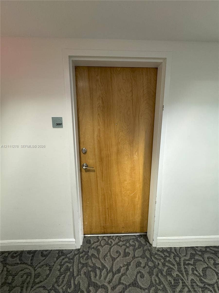 Solid wood-finish door with brushed nickel lever handle and deadbolt, featuring an acrylic wall-mounted suite sign