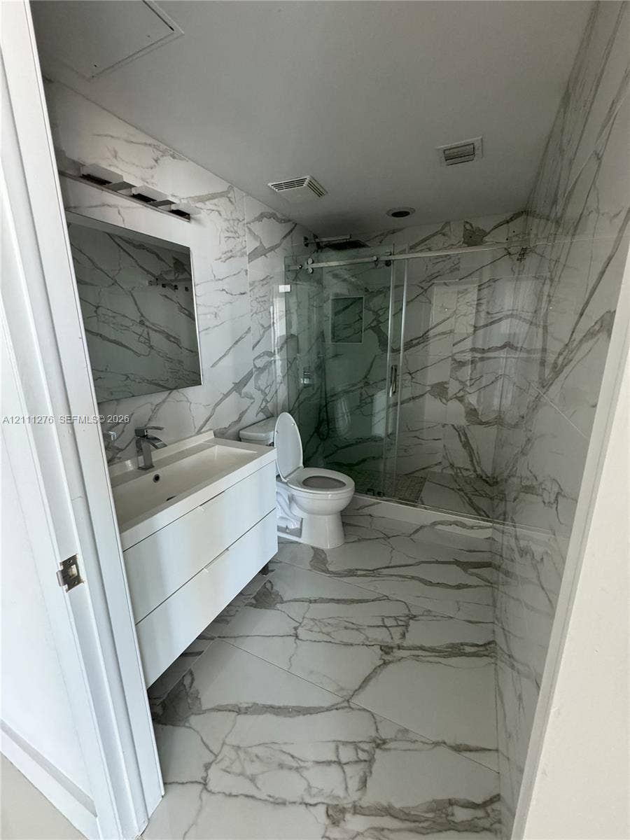 Bathroom featuring large-format veined tile flooring and wall surfacing, a wall-mounted floating vanity with integrated sink, and a glass-enclosed shower with polished metal hardware