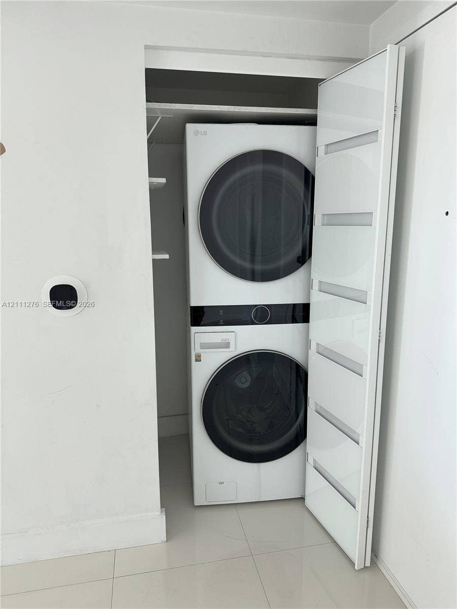 Stacked laundry unit featuring a high-efficiency white finish, sleek door with horizontal glass panels, built-in shelving, and a wall-mounted digital climate control interface