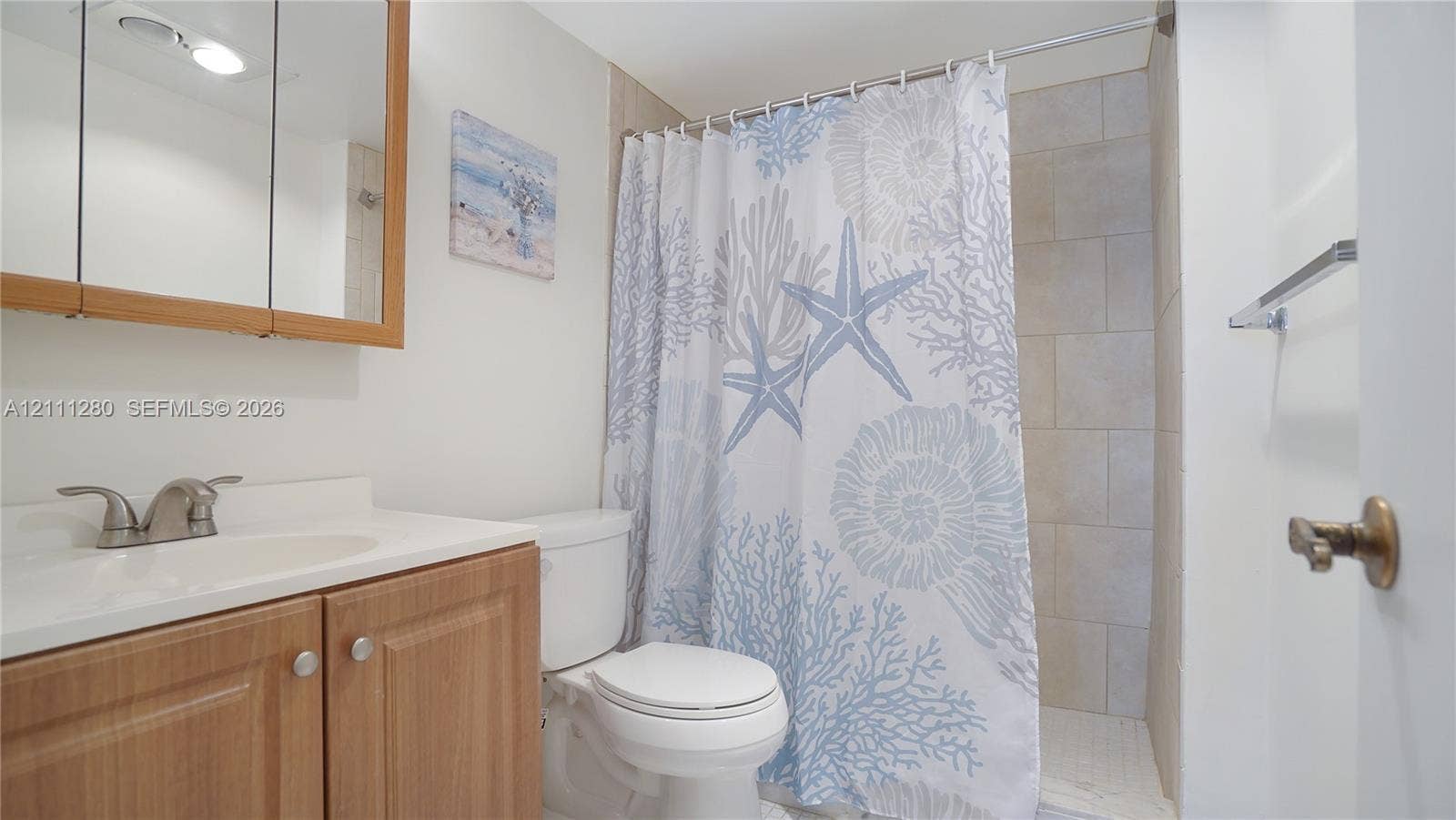 400 N Riverside Drive, #305, Pompano Beach, FL 33062 Wood-finish vanity cabinet with a solid-surface integrated sink, mirrored medicine cabinet, and tiled shower surround