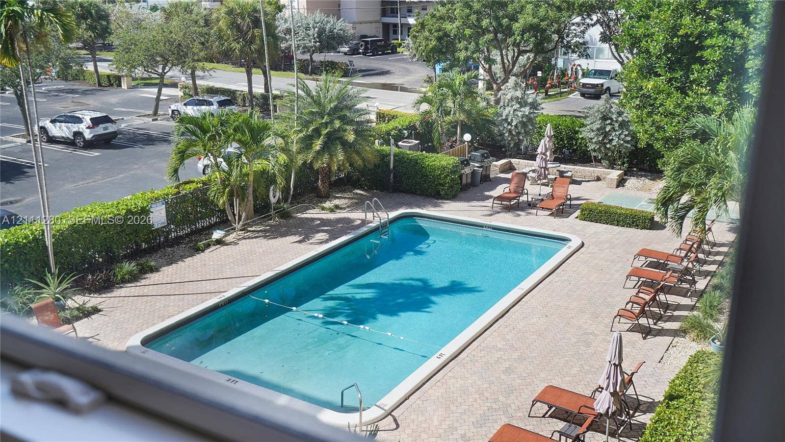 400 N Riverside Drive, #305, Pompano Beach, FL 33062 Rectangular swimming pool featuring integrated ladder entry and stone paver decking surrounded by mature landscaping and perimeter hedging