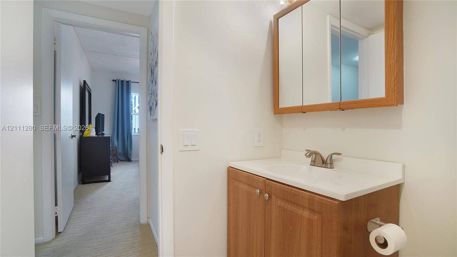 400 N Riverside Drive, #305, Pompano Beach, FL 33062 Wood-finish vanity cabinet, integrated countertop with basin, dual-handle faucet, and wooden-framed mirrored medicine cabinet