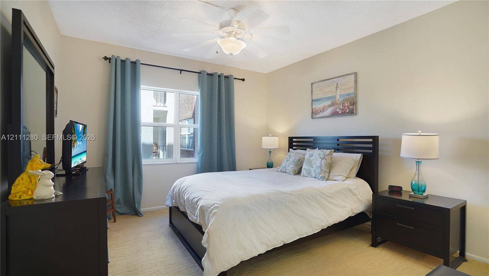 400 N Riverside Drive, #305, Pompano Beach, FL 33062 Neutral-toned interior room featuring wall-to-wall carpeting, a multi-pane window with dark metal curtain rod, and a central ceiling fan with integrated lighting