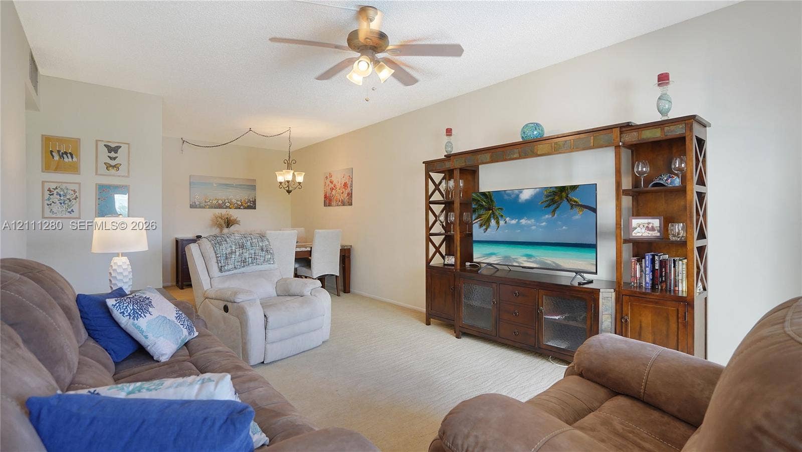 400 N Riverside Drive, #305, Pompano Beach, FL 33062 Living area featuring neutral carpeting, a ceiling fan with integrated lighting, and a multi-tiered decorative light fixture
