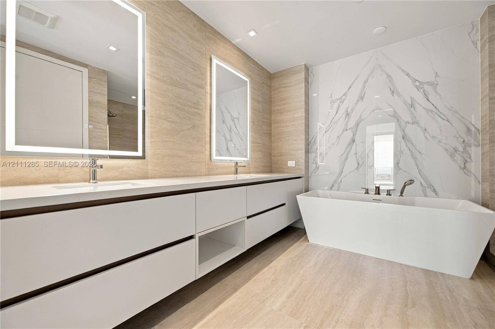Dual-sink vanity with white cabinetry and countertop, backlit rectangular mirrors, freestanding soaking tub, and large-format tile surround