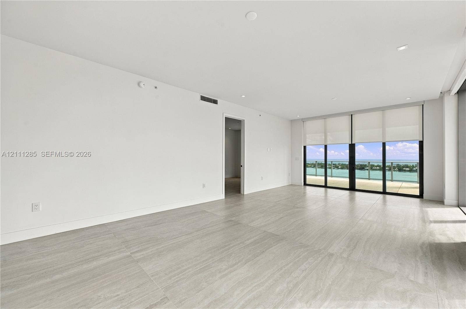 Neutral-toned stone flooring, recessed ceiling lighting, floor-to-ceiling glass sliding doors, and private exterior balcony