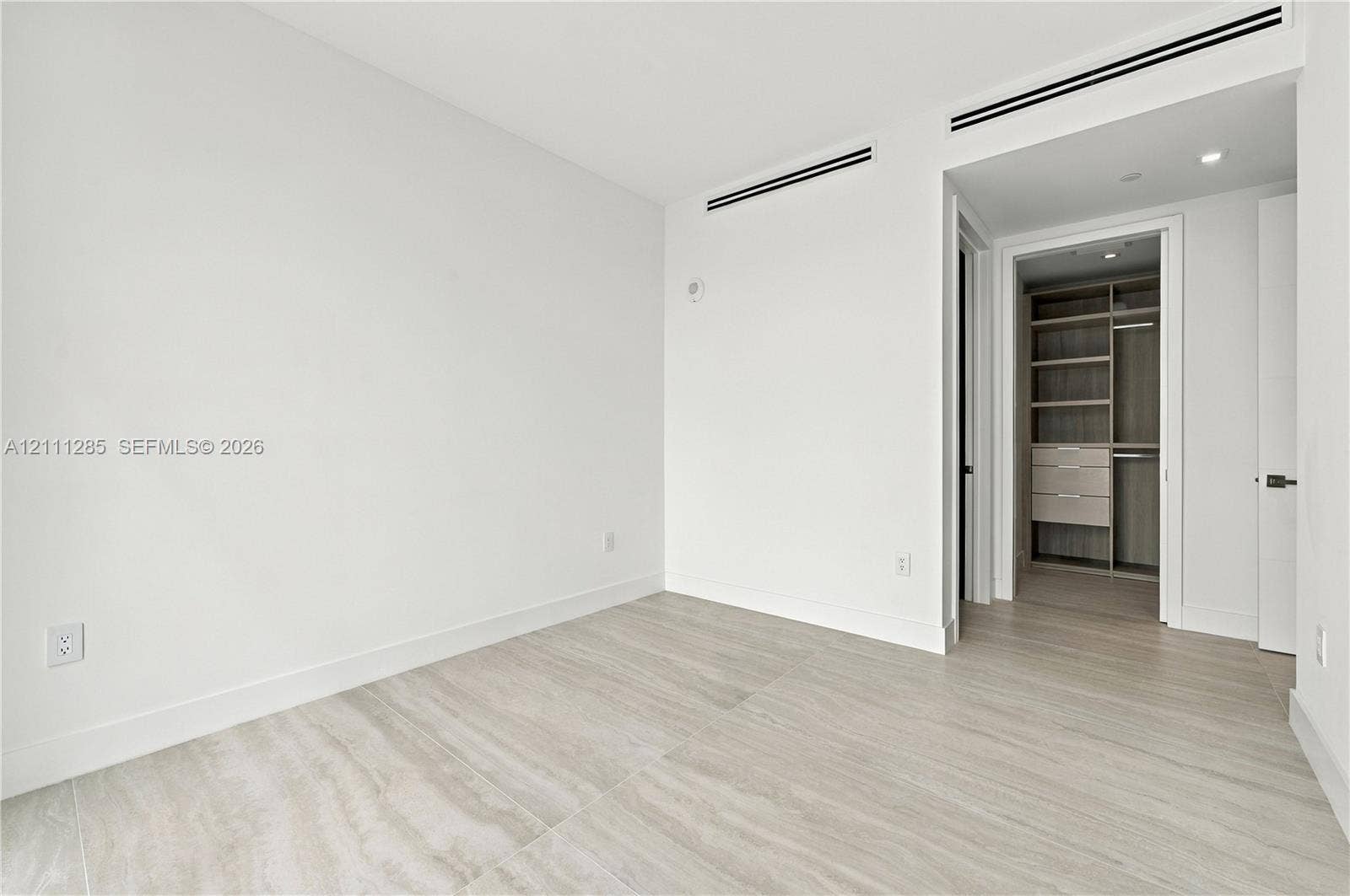Neutral-toned tile flooring, built-in wooden closet system with shelving and drawers, and recessed linear ceiling detailing