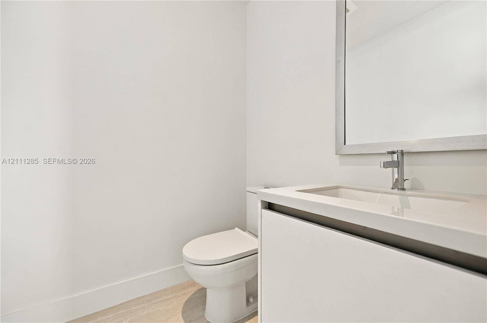 Modern vanity featuring a seamless integrated countertop and sink, wall-mounted mirror with a metallic frame, chrome faucet, and light-toned wood-finish flooring