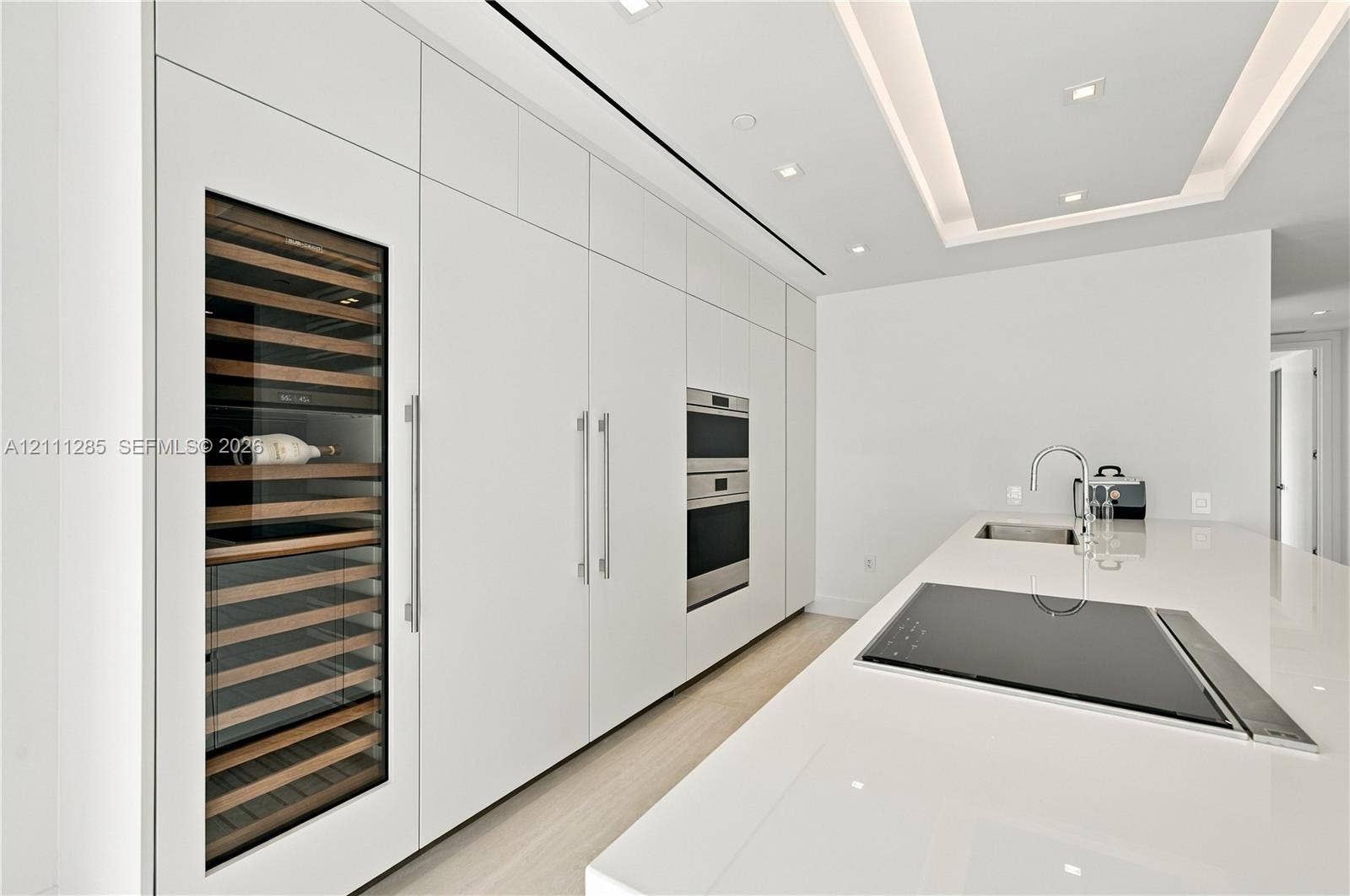 Sleek kitchen featuring custom floor-to-ceiling cabinetry, built-in stainless steel appliances, a glass-front wine refrigerator, and a solid-surface island with an integrated cooktop and undermount sink