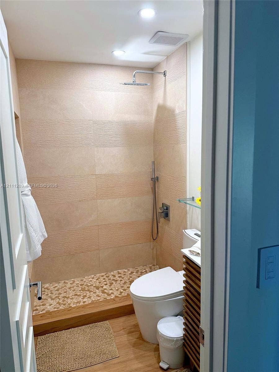 Walk-in shower featuring textured wall tile, pebble-stone flooring, and a rainfall showerhead with a separate handheld sprayer, paired with a wood-slat vanity cabinet