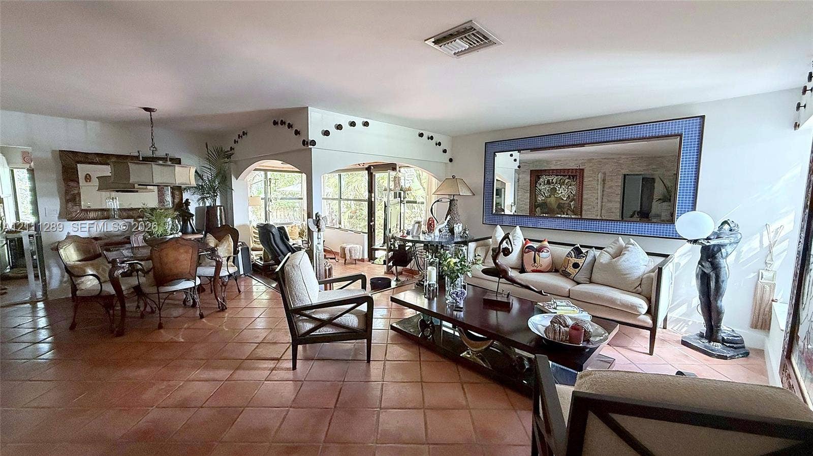 Open living area featuring large-format terra-cotta tile flooring, architectural arched openings, and a large decorative wall mirror with a blue mosaic frame