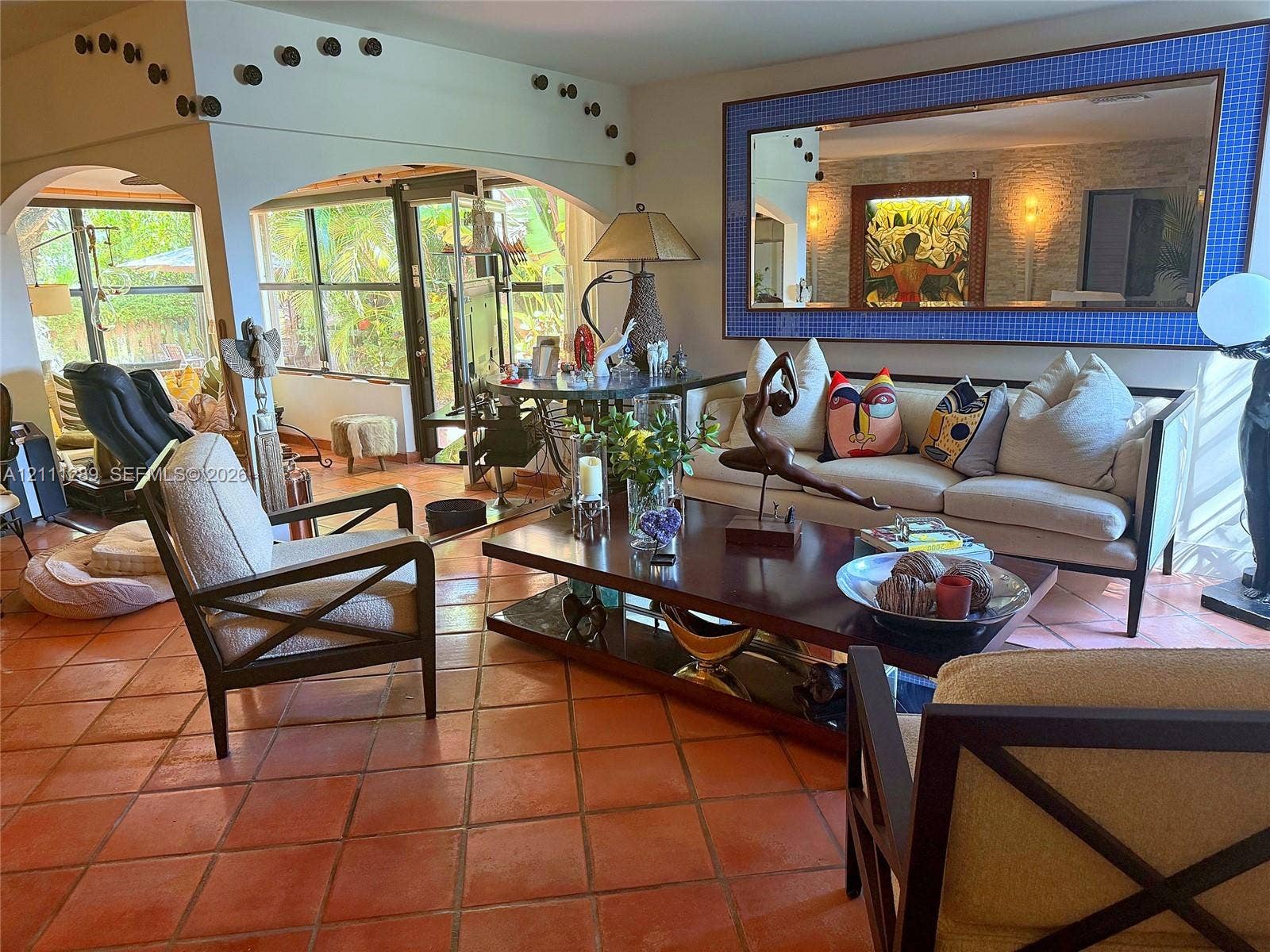 Living area featuring terracotta tile flooring, dual arched wall openings, and a large decorative wall mirror