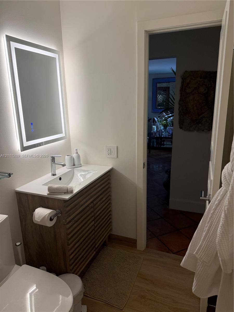 Wood-finish slatted vanity with a white countertop and integrated sink, paired with a modern LED-backlit mirror and a polished chrome single-handle faucet