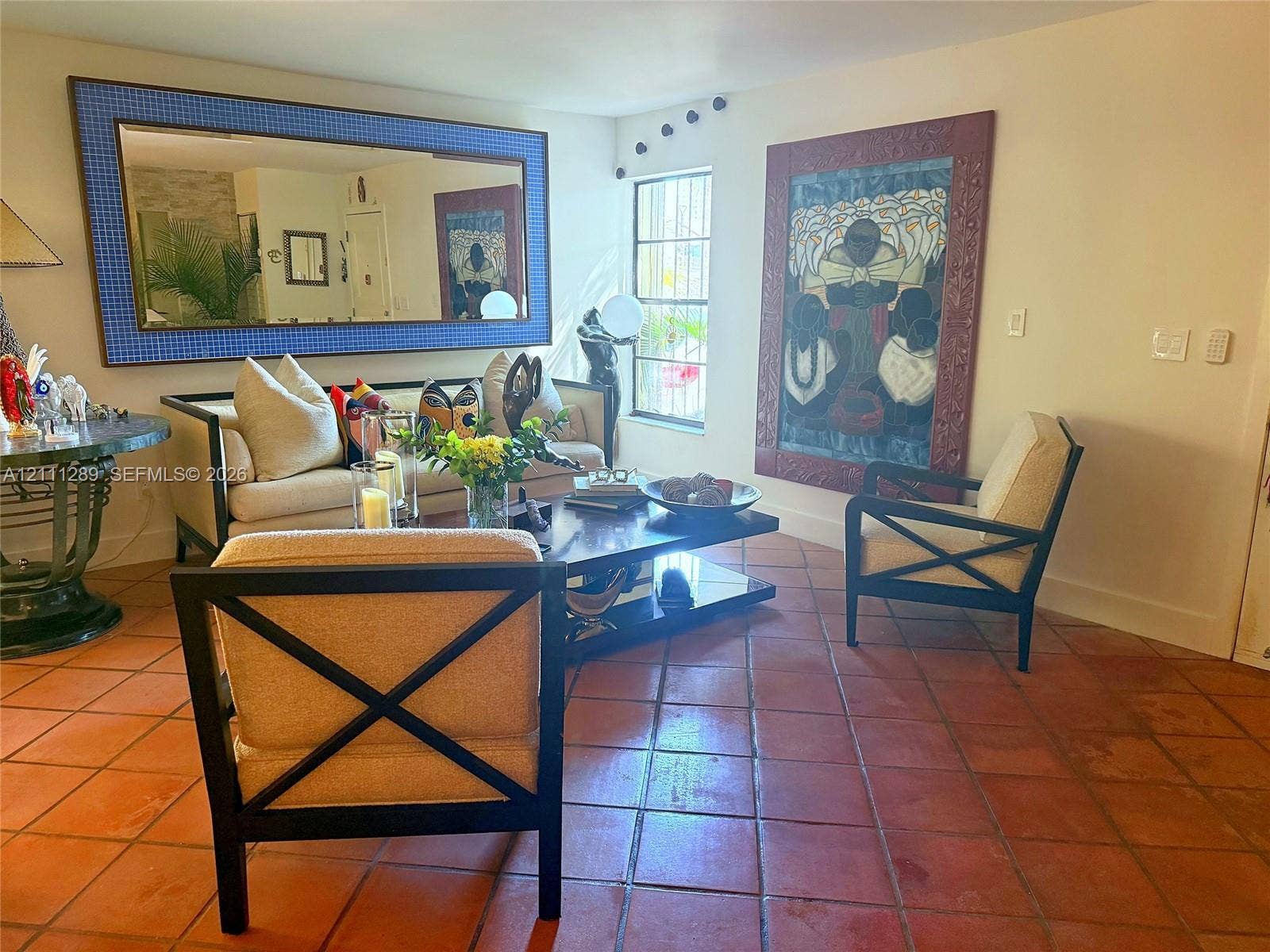 Terracotta tile flooring, large-format rectangular wall mirror with a textured blue frame, and multi-pane window with security bars