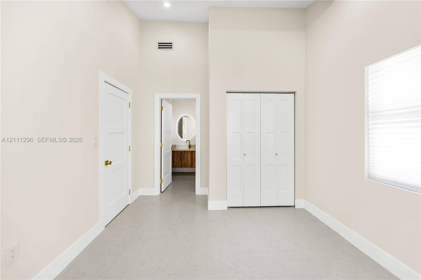 High-ceilinged room featuring neutral wall tones, large-format tile flooring, double-door closet cabinetry, and three-panel interior doors