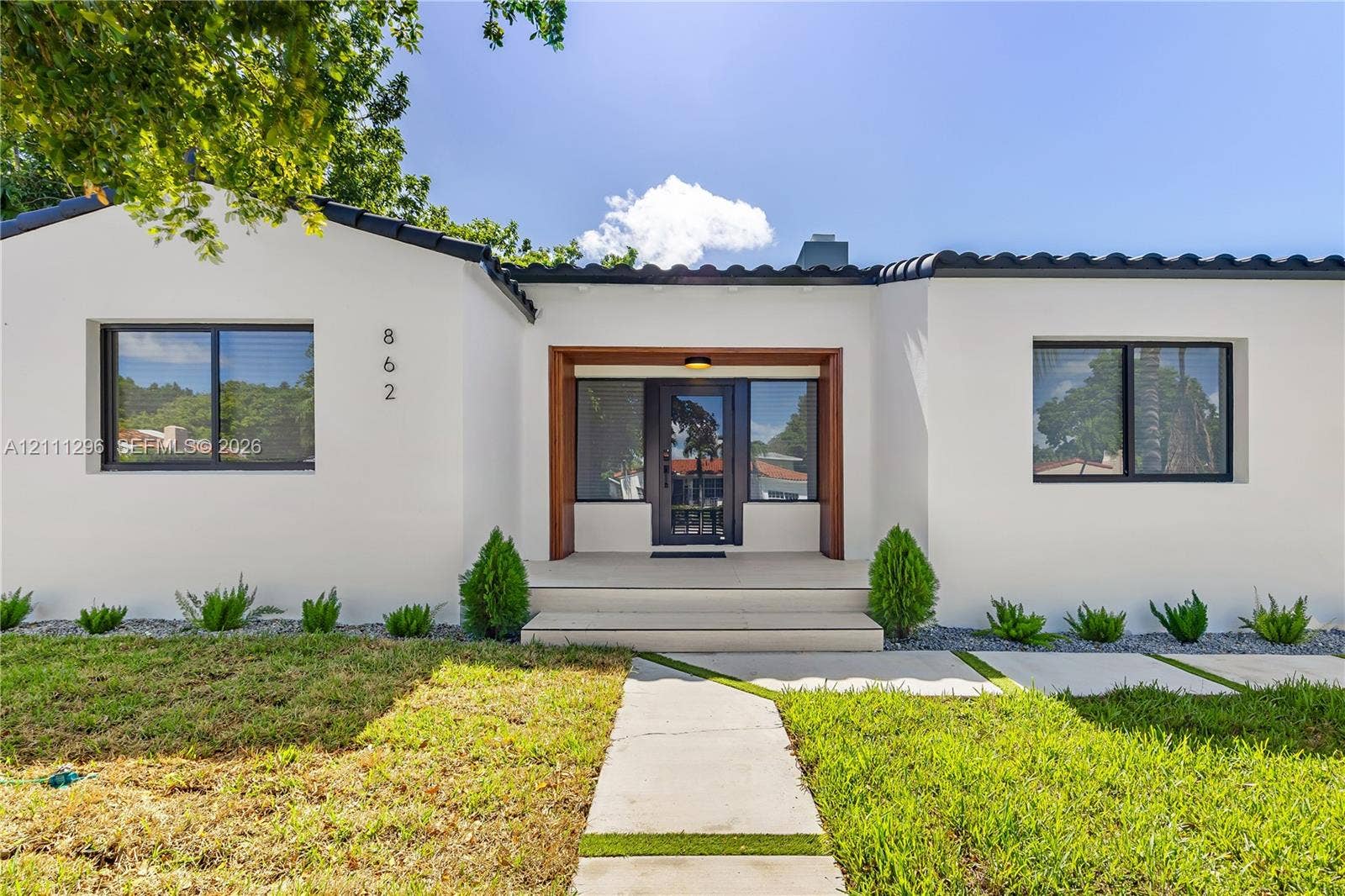 Stucco exterior featuring dark-trimmed windows, a flat tile roof, a wooden-framed entry, and a concrete paver walkway