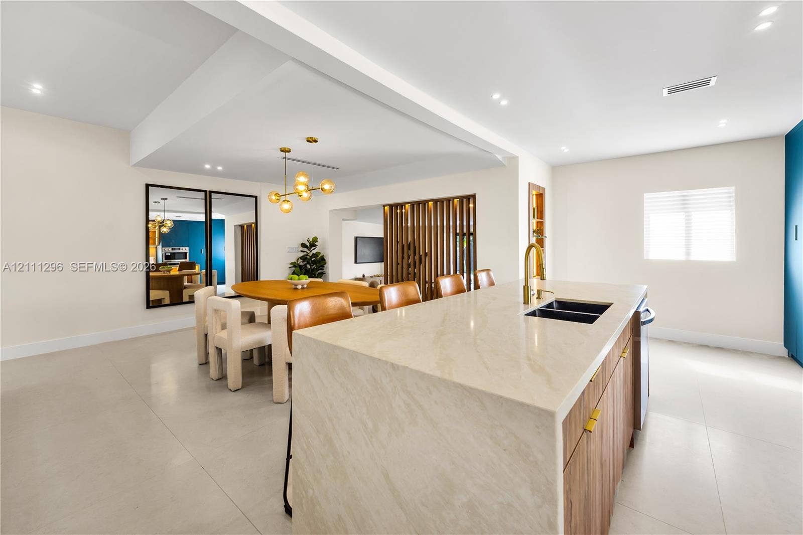 Kitchen island with waterfall countertop, wood-finish cabinetry, brass-toned faucet, recessed lighting, and decorative wood slat partition