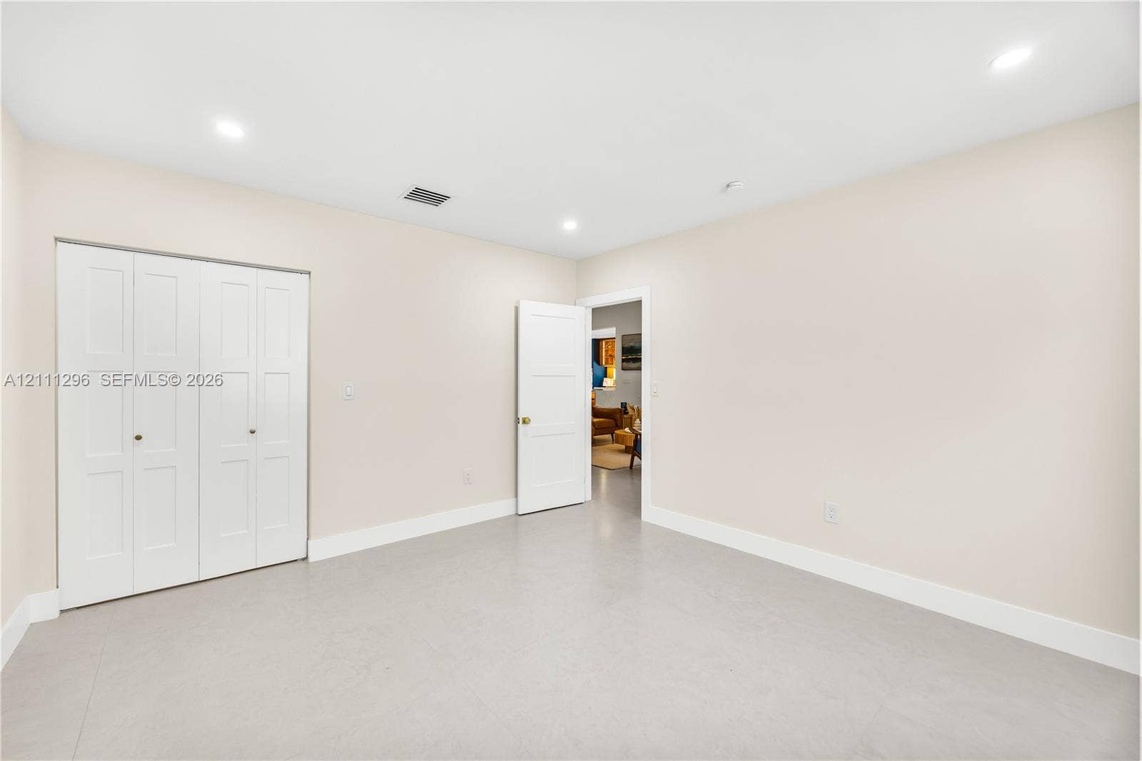 Neutral-toned interior room featuring recessed lighting, a three-panel door, and a white bi-fold closet