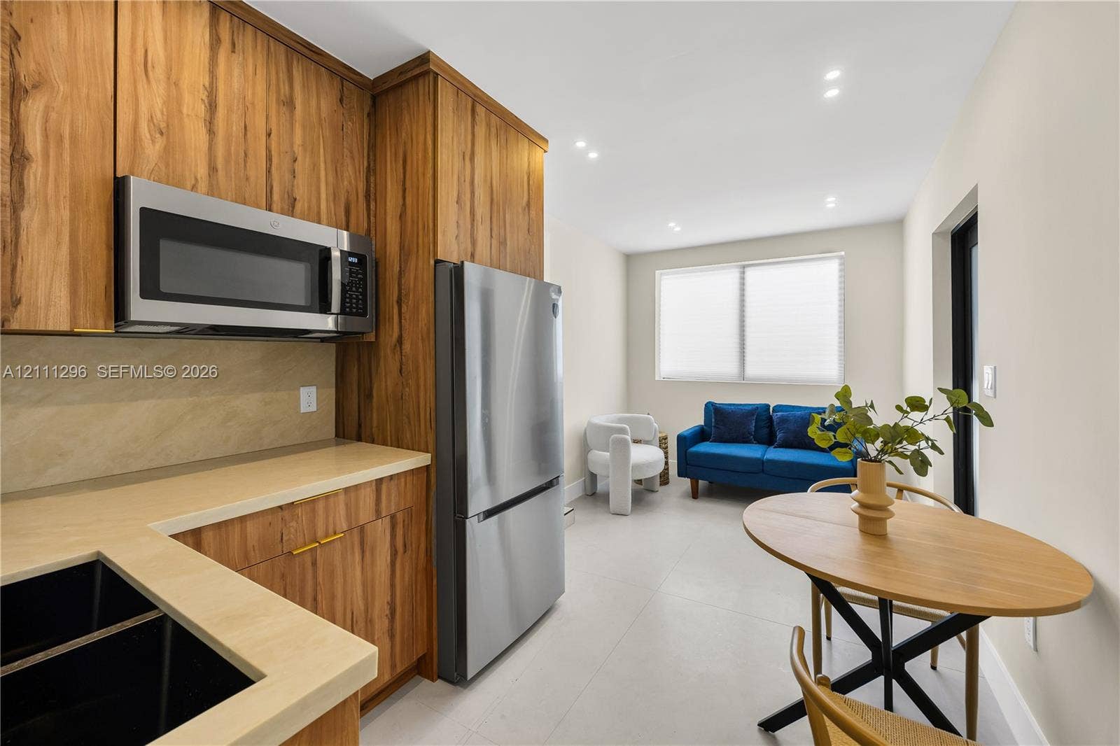 Kitchen featuring wood-finish cabinetry, stainless steel appliances, a solid-surface countertop, recessed ceiling lighting, and large-format tile flooring