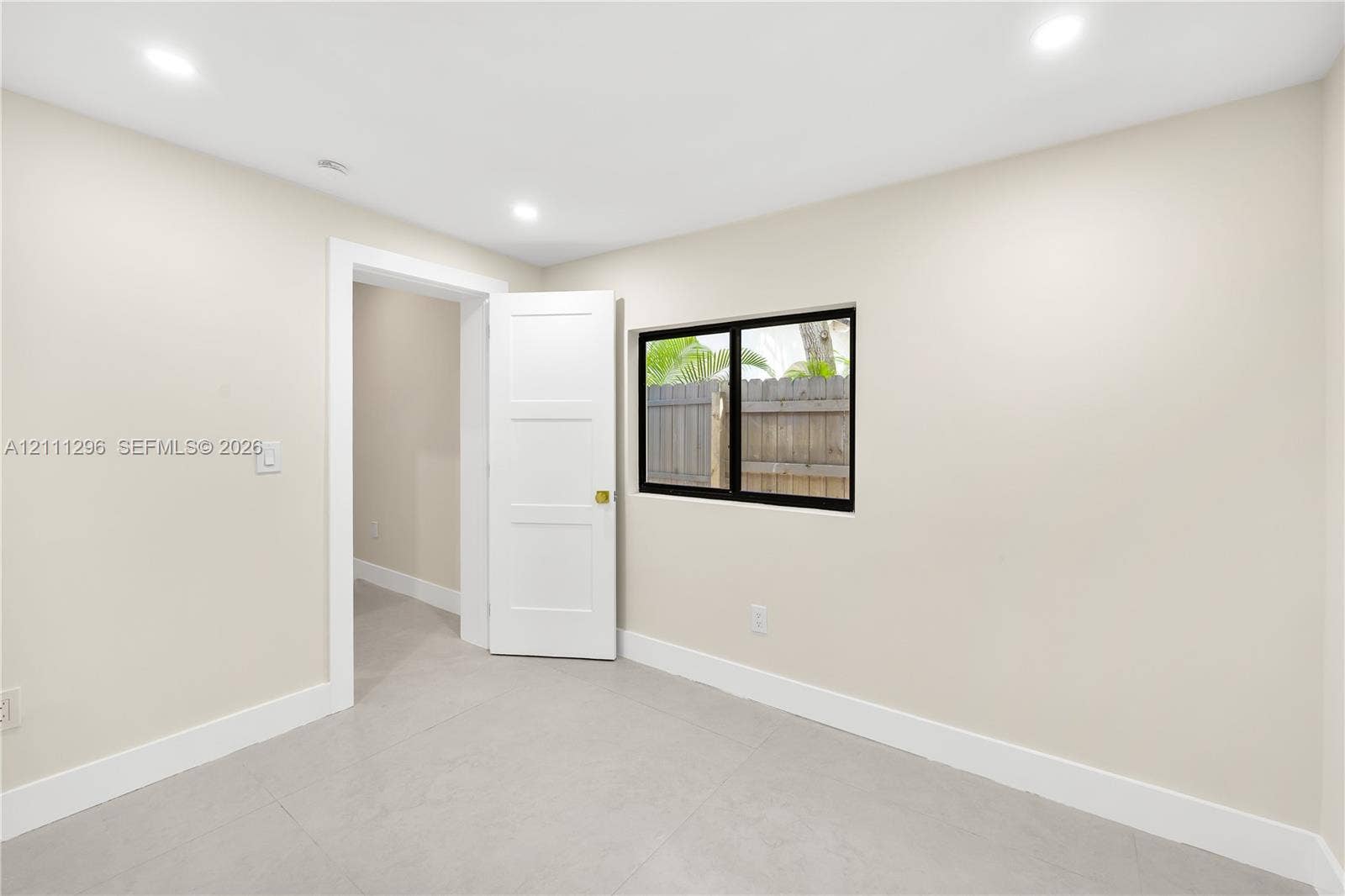 Neutral-toned interior space featuring tile flooring, recessed ceiling lighting, a three-panel interior door, and a black-framed window