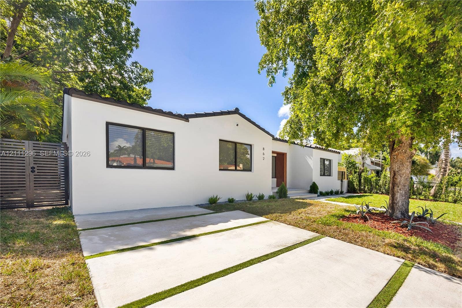 Stucco exterior featuring dark-framed windows, a concrete ribbon driveway with turf accents, and a horizontal slat privacy gate