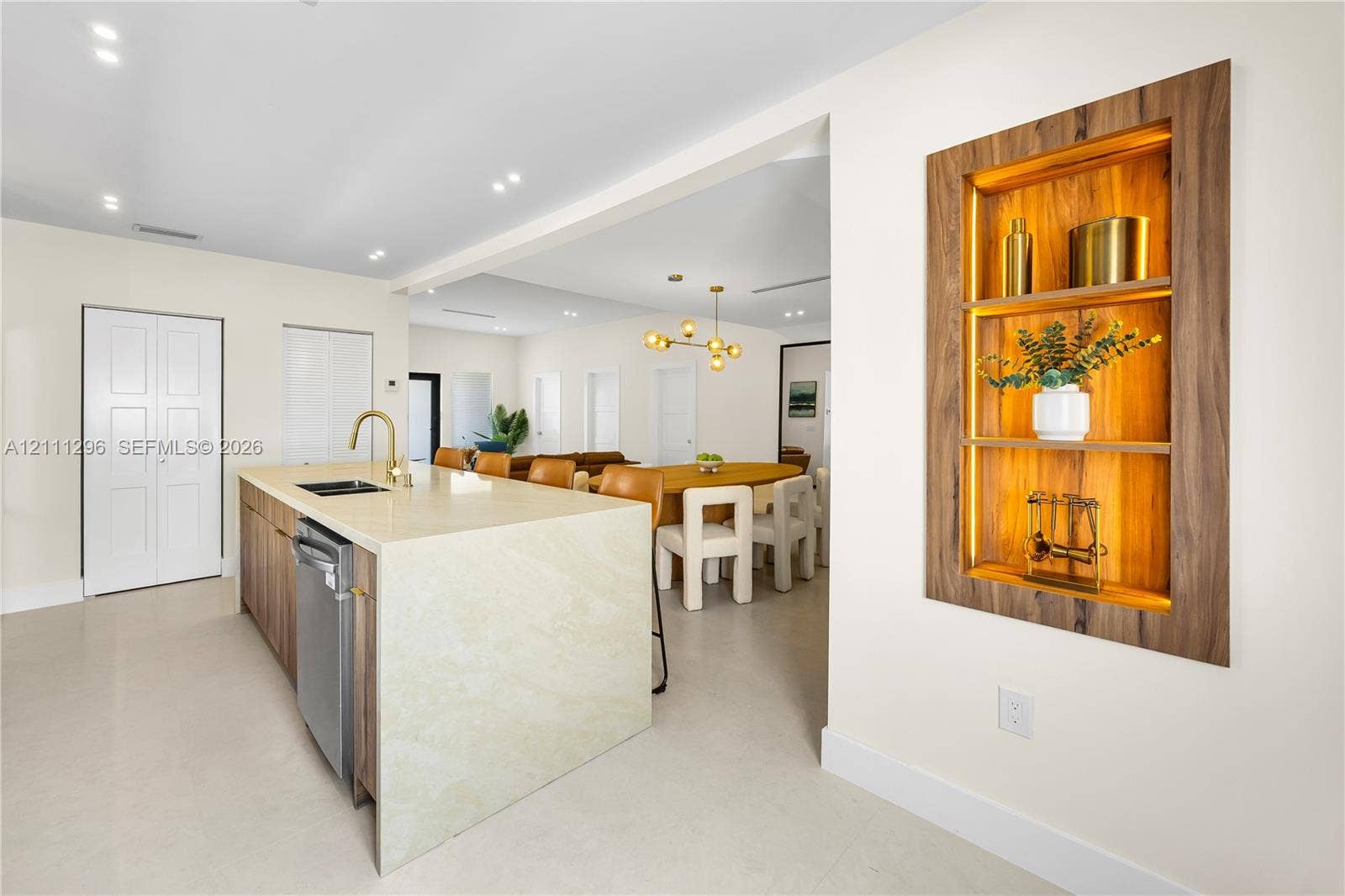Kitchen island featuring a waterfall stone countertop, integrated stainless steel dishwasher, and a gooseneck faucet, accompanied by a recessed wall niche with wood-finish trim and integrated backlighting