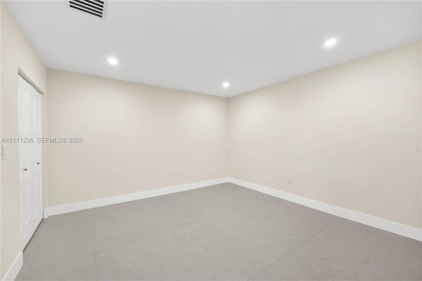 Neutral-toned room featuring large-format tile flooring, recessed ceiling lighting, and a dual-panel closet door