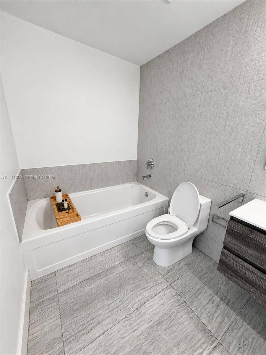 1111 SW 1st Avenue, #2324-N, Miami, Miami, FL 33130 Bathroom featuring a deep soaking tub, large-format textured tile flooring, full-height wall tiling, and a floating vanity with a stone countertop