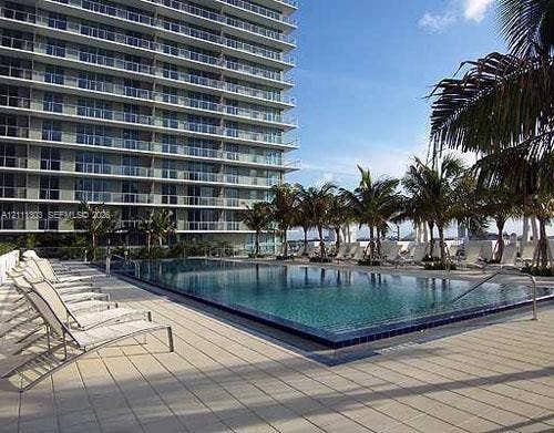 1111 SW 1st Avenue, #2324-N, Miami, Miami, FL 33130 Infinity-edge swimming pool featuring a tiled waterline, surrounded by a paved deck with mature palm trees and a multi-story glass balcony exterior