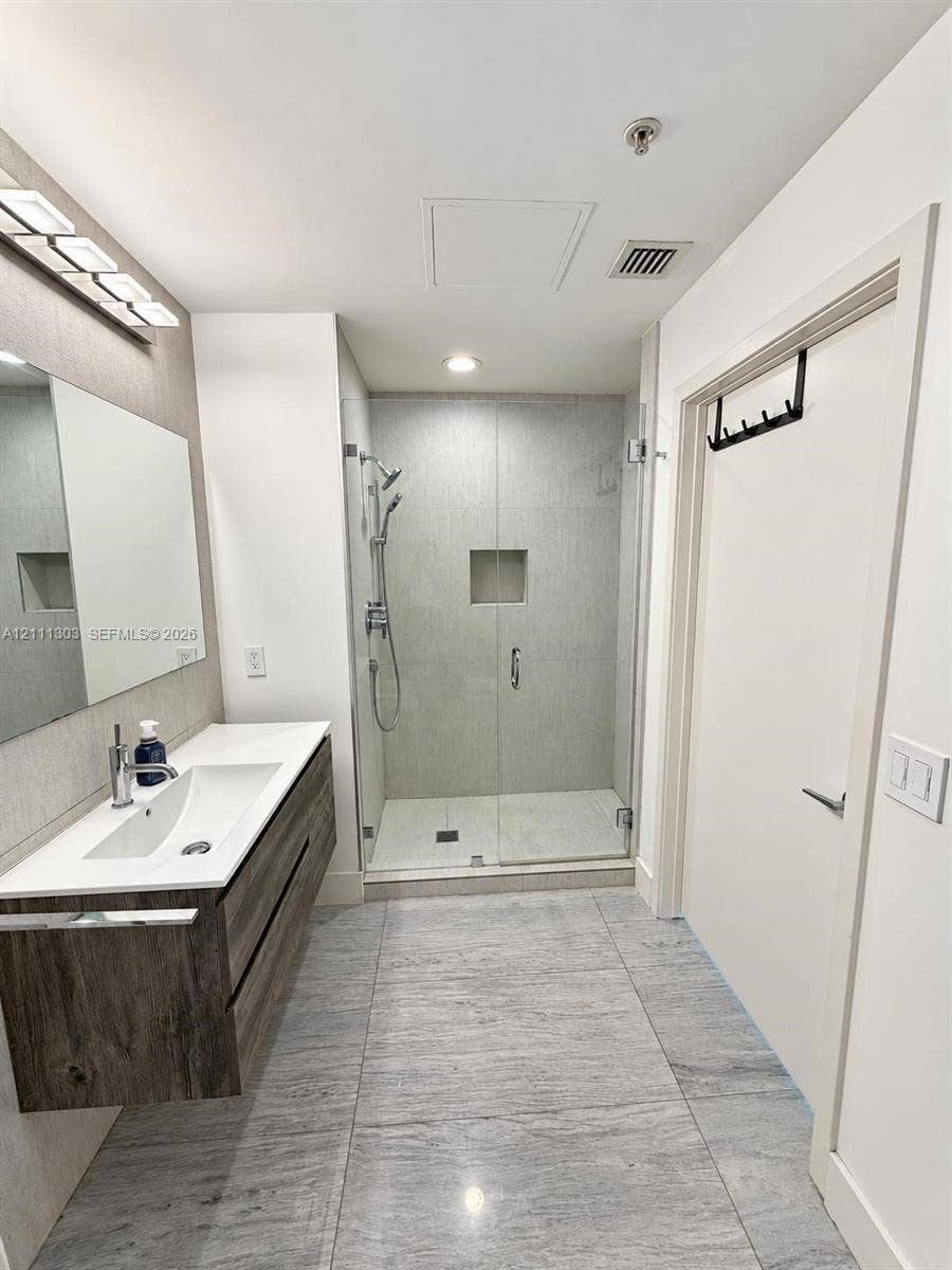 1111 SW 1st Avenue, #2324-N, Miami, Miami, FL 33130 Floating wood-finish vanity with integrated sink, stone-composite countertop, glass-enclosed shower with tiled surround, and large-format tile flooring