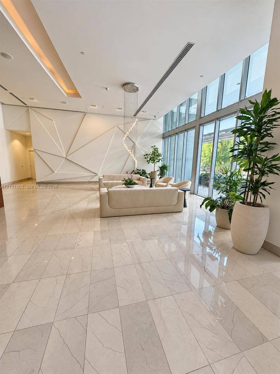 1111 SW 1st Avenue, #2324-N, Miami, Miami, FL 33130 Grand entrance lobby featuring expansive floor-to-ceiling windows, polished stone tile flooring, a custom geometric accent wall, recessed architectural lighting, and a sculptural hanging pendant light