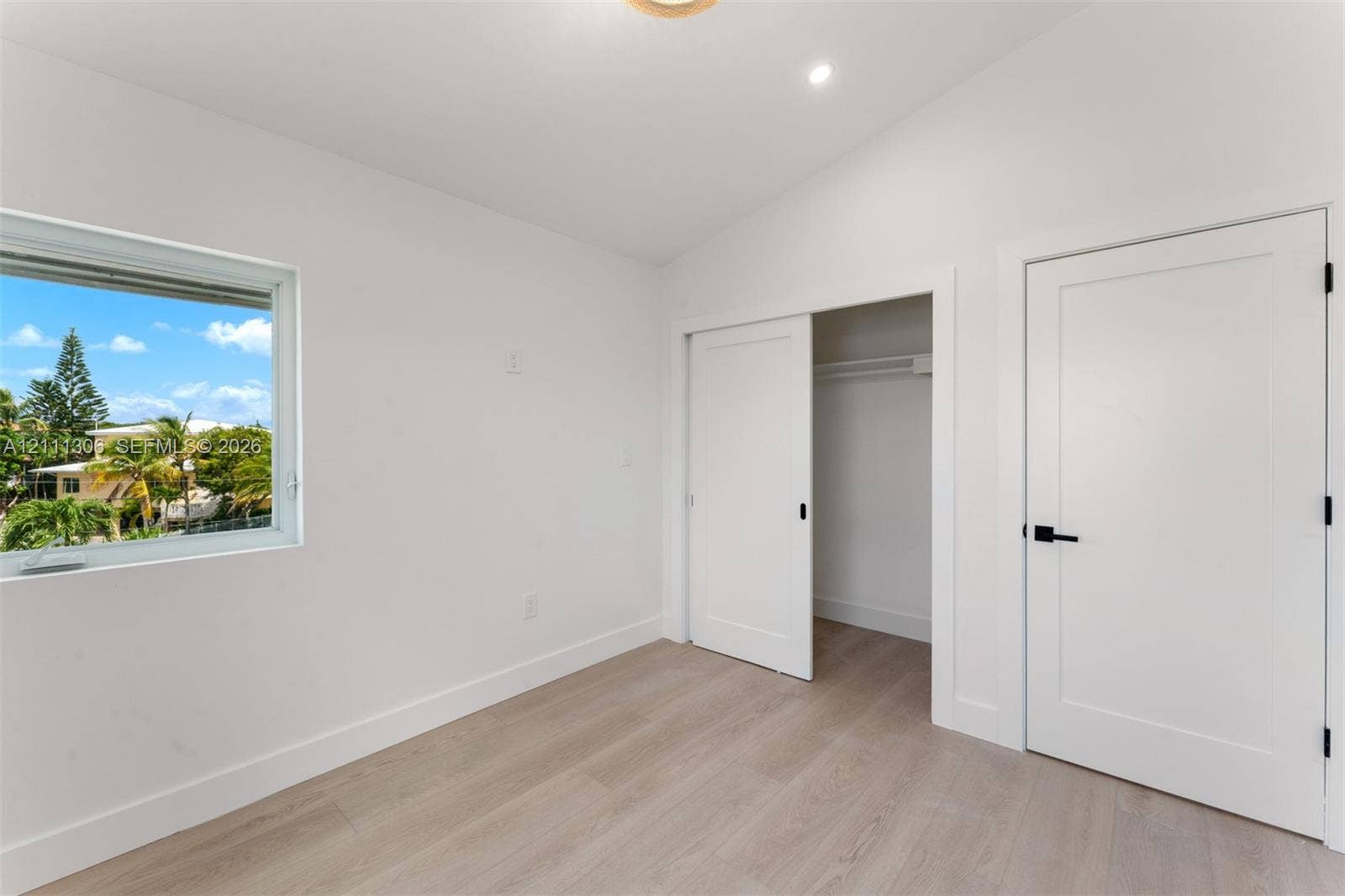 Interior space featuring vaulted ceilings, light-toned wood-finish flooring, a sliding closet door, and a single-panel interior door with matte black hardware